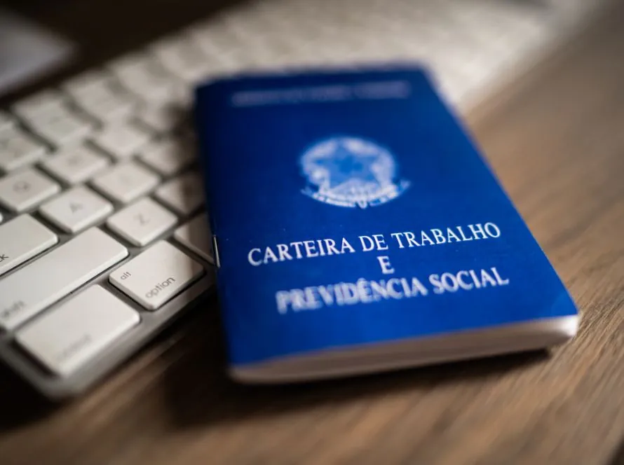 Carteira de Trabalho e Previdência Social ao lado de um teclado, ilustrando a mudança na jornada e na escala 6x1